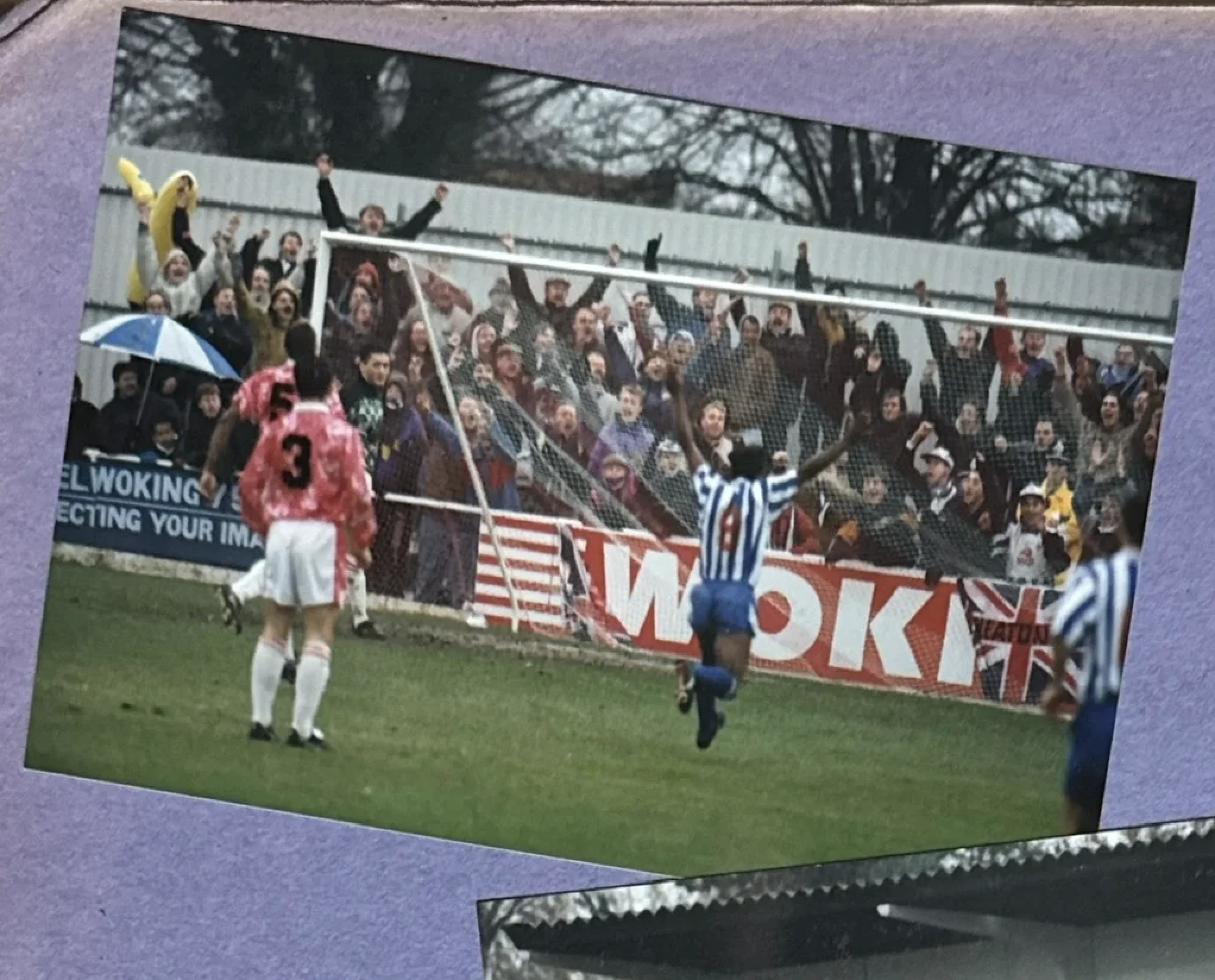 Nuneaton Borough player in blue and white stripes celebrates a goal in front of a jubilant crowd
